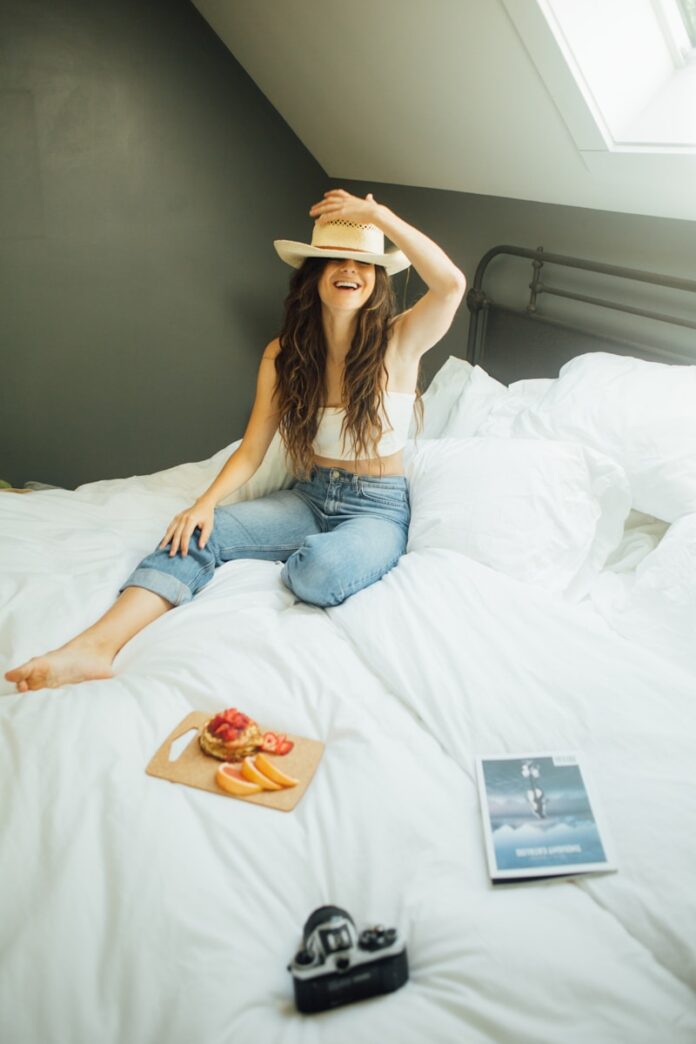 Photo by Thought Catalog woman sitting on bed holding her hat