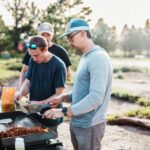 바쁜 일상 속 ‘마음 챙김 식사’ 실천법…행복한 식탁 만드는 작은 습관들 Three men cooking food on an outdoor grill.