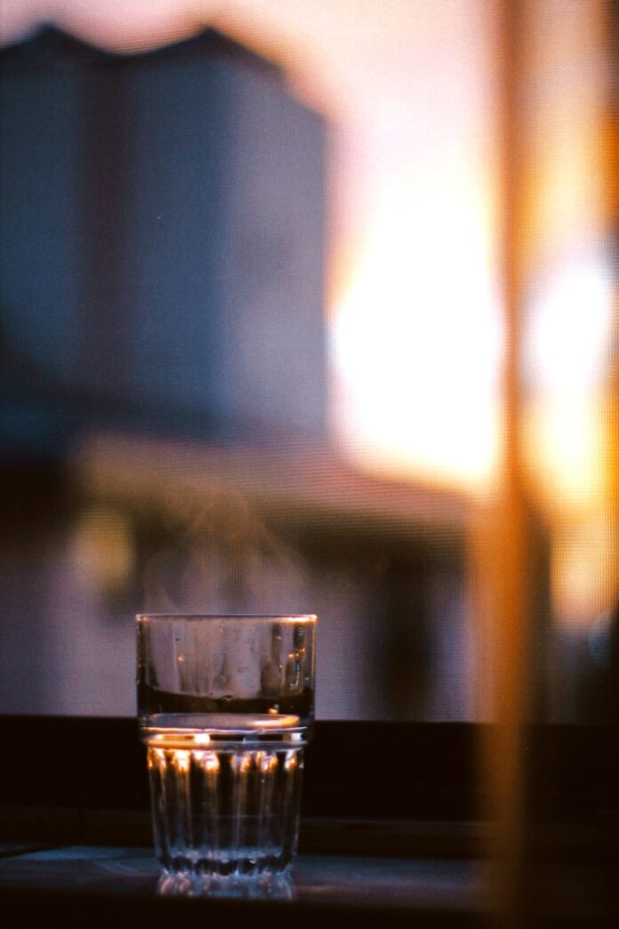 Photo by X Du a glass of water sitting on a window sill